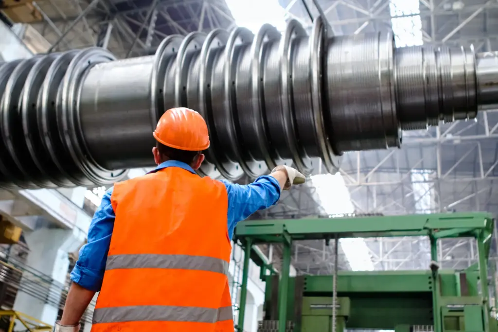 Engineer in high-visibility vest and hard hat inspecting large machinery at an industrial facility